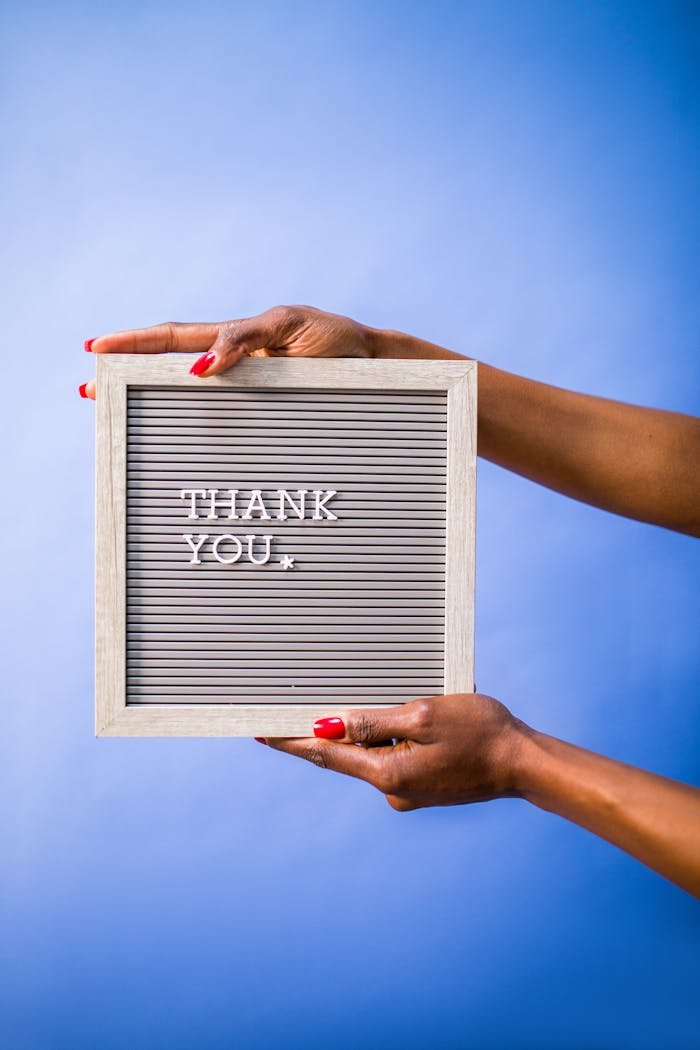 Hands holding thank you sign on blue backdrop, perfect for social media and digital marketing.