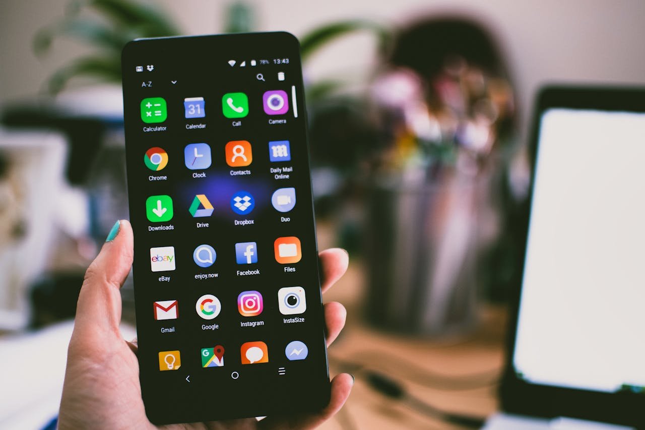 A close-up image of a persons hand holding a smartphone displaying various popular apps.